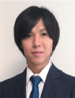 A photograph of a man with dark hair wearing a dark suit jacket and a light shirt with a striped tie.