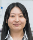 A photograph of a woman with long dark hair wearing a striped collared shirt.