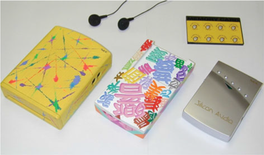 A photograph showing a patterned box, a colorful printed card, a gold box, a small device, and two earphones.
