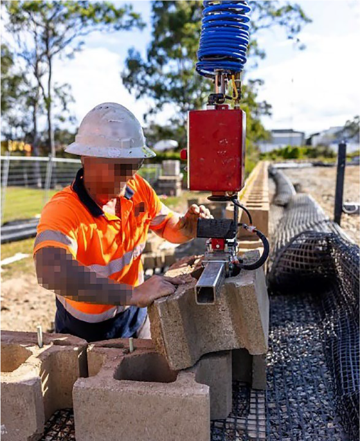 A construction worker positions a large block with the help of an collaborative robotic arm on a masonry site.