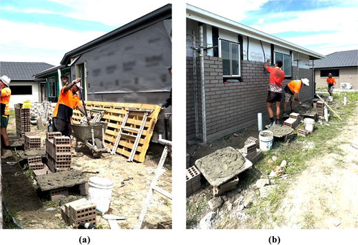 Construction workers build an exterior brick wall for a residential house using mortar and stacked bricks.