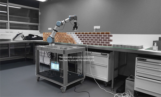 A robotic arm beside a brick wall displays a digital overlay of a wall segment, with on-screen text indicating the assembly process is completed and relocation is possible.