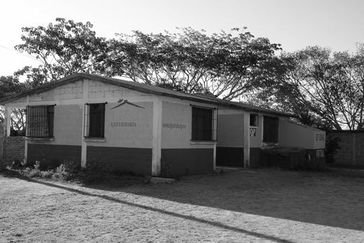 A photograph of a one-story rectangular building with a covered porch and barred windows.