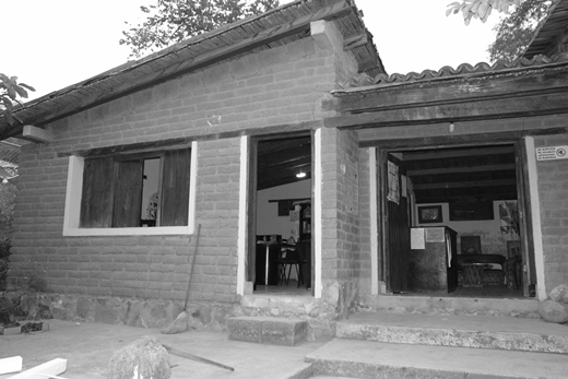 A photograph of a small building made of unpainted brick and a thatched roof.
