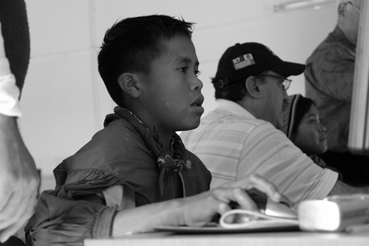 A photograph shows a young male in the foreground seated at a desk.