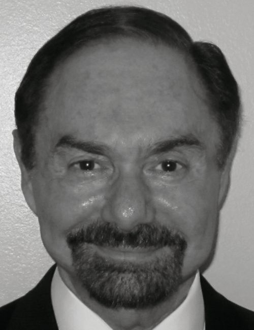 Smiling man with dark hair and beard, wearing a suit. Black and white portrait with close-up framing against a plain background.