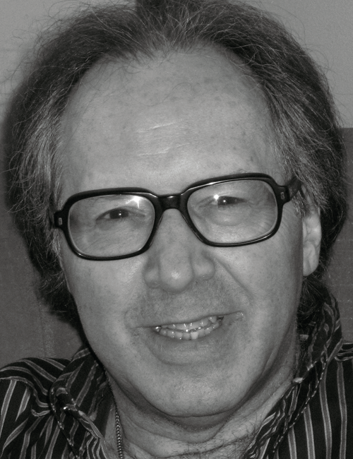 Black and white photo of a smiling older man with glasses and wavy hair, wearing a striped shirt. The tone is warm, conveying friendliness.