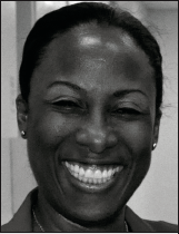 A black and white photo of a person smiling broadly. The expression conveys warmth and happiness. The background is blurred, keeping focus on the face.