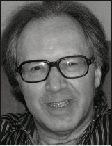 Black and white image of a smiling middle-aged man with glasses, wearing a striped shirt. His expression conveys warmth and friendliness.