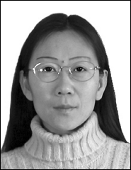 A woman with long dark hair and glasses wears a light-colored turtleneck sweater and looks directly at the camera against a plain background.