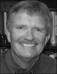 A monochrome photograph of a man sporting a mustache, captured in a thoughtful pose, emphasizing his facial features.
