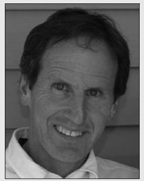 A black and white portrait of a man smiling, reflecting a cheerful and approachable personality.