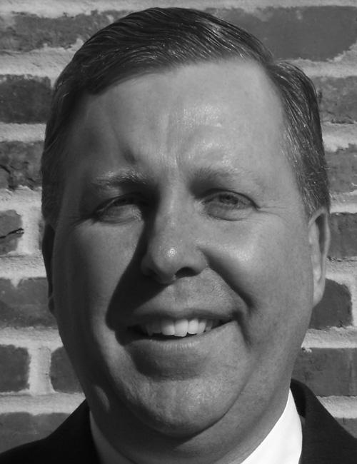 Black and white photo of Michael Corry in front of a brick wall, with text listing his role at George Washington University, office address in Washington, DC, and email contact.