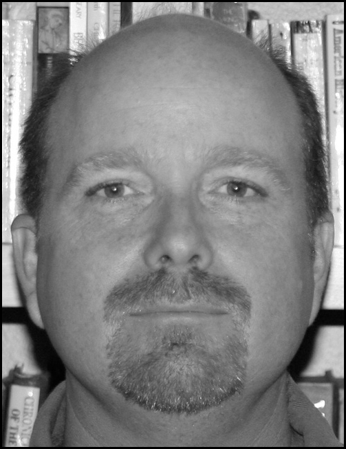 Black and white photo of Daniel Prouty in front of a bookshelf.