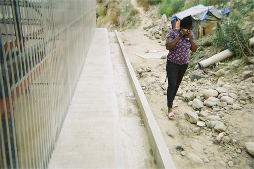 A photograph of a person taking a picture on rocky ground beside a long reflective wall.