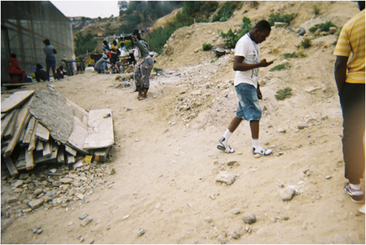 A photograph of people on a dirt slope near piles of wood and rubble, with others gathered by tables in the background.