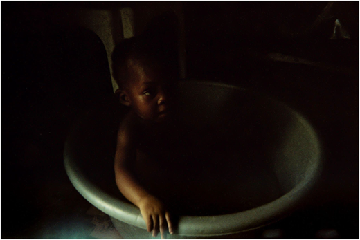 A photograph of a child sitting in a round tub in a dimly lit space.
