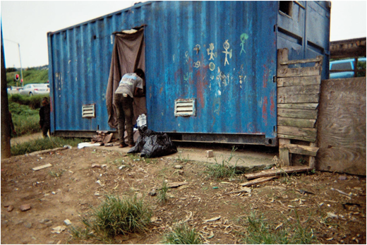 A photograph of a container with drawings on its side, a person entering through a cloth-covered doorway.