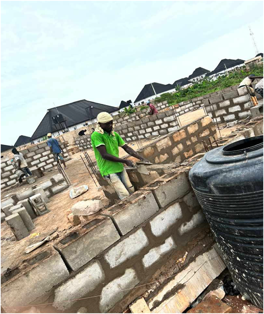 A photograph of a worker in a green shirt applying mortar to concrete blocks at a construction site without protective gear.