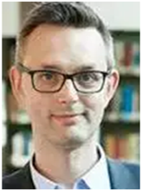 A photograph of Tilo Halaszovich, in glasses and formal attire, smiling at the camera. A bookshelf is present in the back.