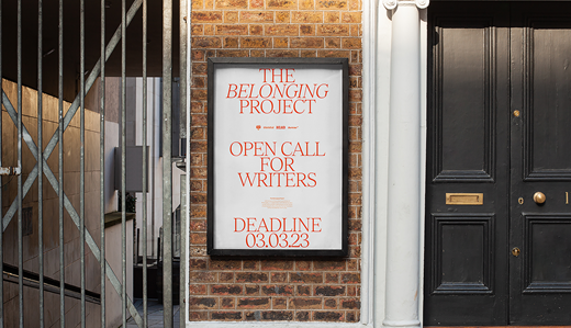 A street display board advertises The Belonging Project open call for writers with a submission deadline of 03.03.23.