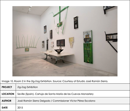 A table with a photo shows green sculptures and framed artworks in a contemporary exhibition space.