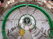 Segment-lined tunnel interior under construction with circular support rings and suspended fittings.