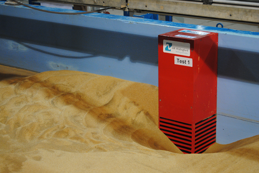 A laboratory view shows a Test 1 block partially embedded in a sand bed inside a flume.