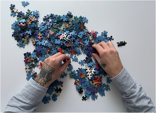 A photograph of hands sorting and assembling scattered jigsaw puzzle pieces on a table.