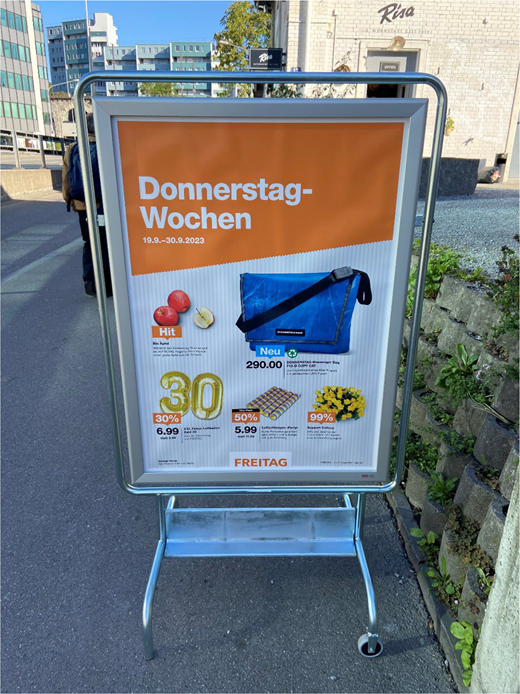 A freestanding pavement sign advertising Donnerstag Wochen from 19.9.2023 to 30.9.2023, featuring discounted products and a messenger bag priced at 290.00.