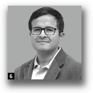 A man with short hair and glasses, wearing a collared shirt and a jacket.