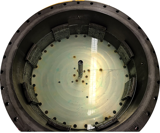 A circular chamber contains a central vertical tube, base plate, perimeter fasteners and components around the inner wall.