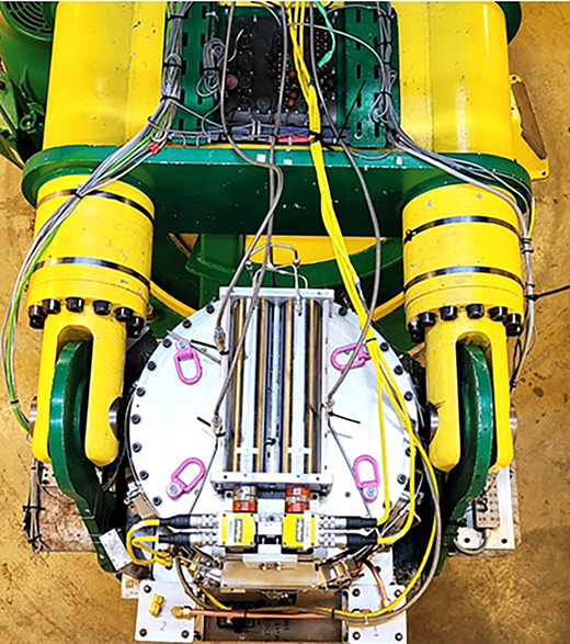 A mechanical test assembly contains a circular chamber, parallel cylinders, sensors, cables, fittings and two supporting arms.
