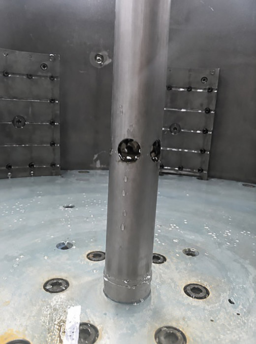 A close-up of a cylindrical metal pipe with two drilled holes, surrounded by a circular base with multiple fastener holes.