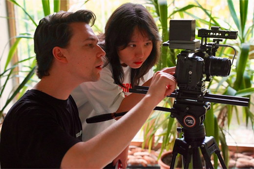 A man and a woman focus intently on a camera on a tripod.