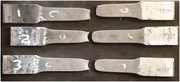 Three fractured metal tensile specimens, labelled 1, 2, and 3, are arranged in rows with separated halves and visible necking.