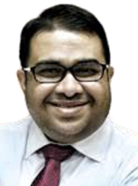 A head shot of a male wearing glasses, a light blue shirt, and a red tie, facing forward and smiling.