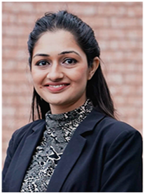 A woman in a black blazer and patterned top smiling.