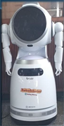 A service robot labelled RoboScholar, with a large circular display, two articulated arms and a wheeled base.