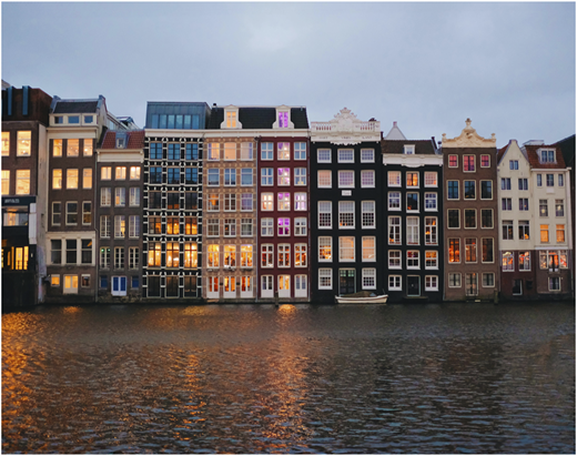 A photograph shows colorful canal-side townhouses reflected in rippling water at dusk.