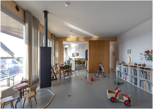 A photograph shows a bright open-plan living space with timber detailing, large windows, and a child riding a small bicycle.