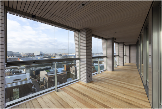A photograph shows a long glazed balcony with timber flooring overlooking a canal-side cityscape.