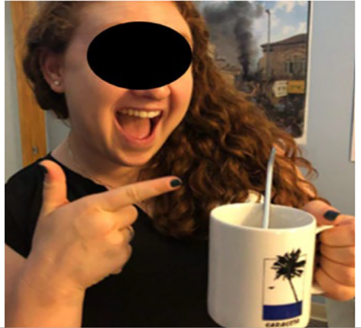 A person with curly hair smiles and points at a white mug with a straw.