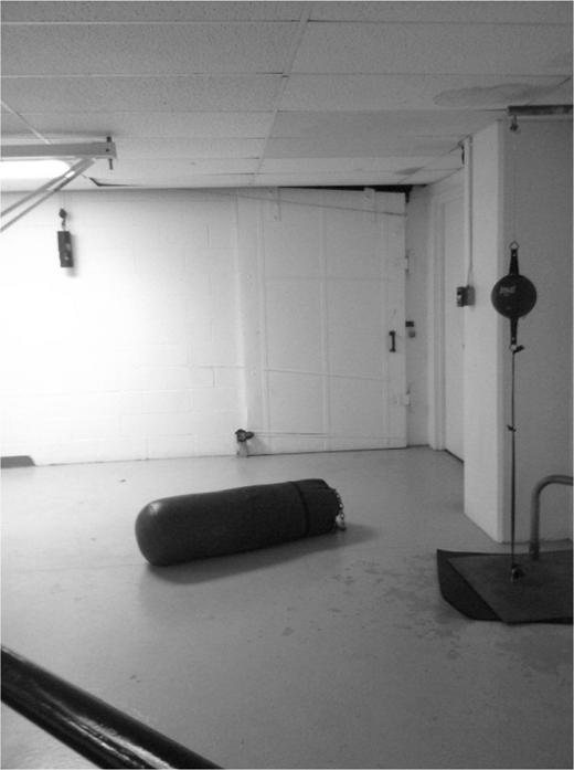 A room with plain walls and a ceiling, a large cylindrical object on the floor, and a tall stand with a spherical object near a closed door.