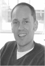 A black and white portrait photo of a smiling middle aged man with short hair and a dark shirt.