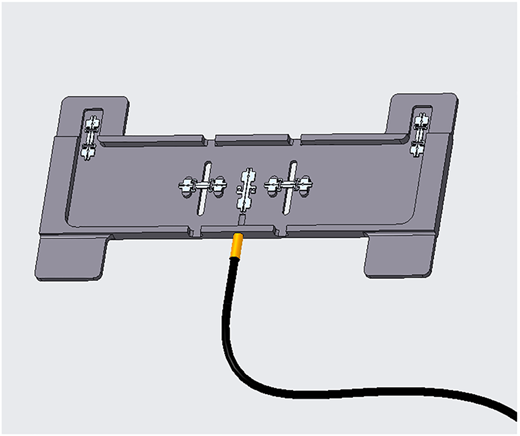 A gray I-beam with slots and mounted hardware, with an attached black cable with a gold connector extending outward.