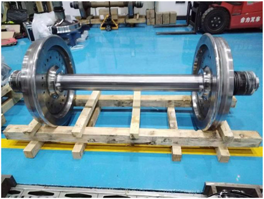 A photograph shows a polished metal wheelset with two wheels on a wooden pallet.