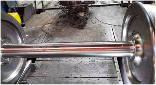 A photograph shows a polished metal wheelset axle mounted on a test stand.