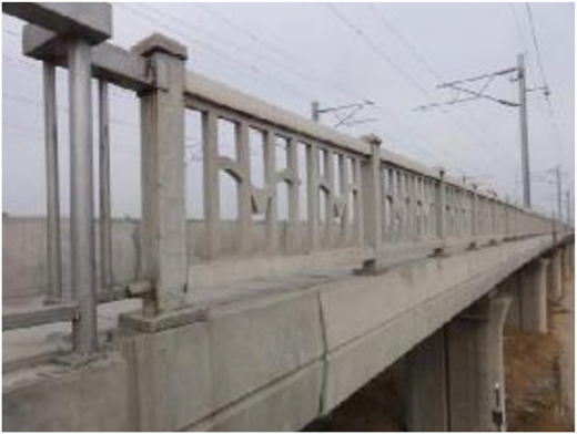 A concrete railway bridge with side railings and overhead electric lines extending into the distance.